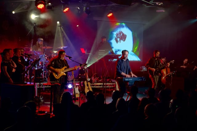 The full band with singers and string players on stage, a tree projected on the screen behind them