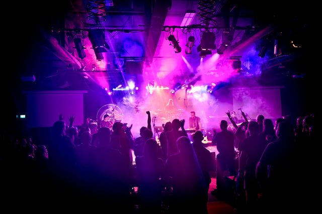 Fans raising their hands toward a stage washed in purple and pink light